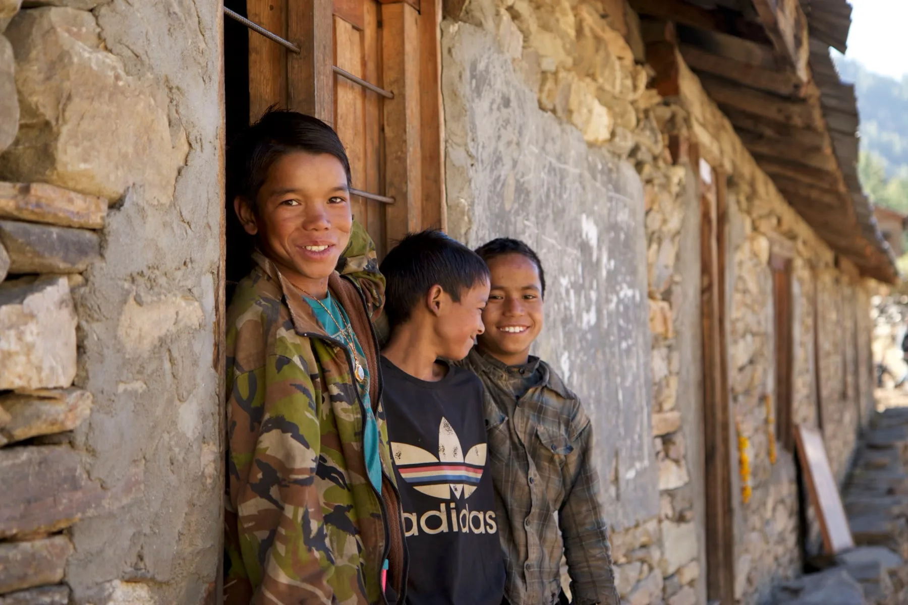 Three boys leaning against a stone wall in a Gyangphedi village